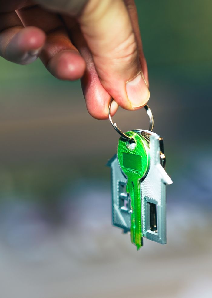 Close-up of a hand holding a house-shaped keychain with green keys, symbolizing home ownership.